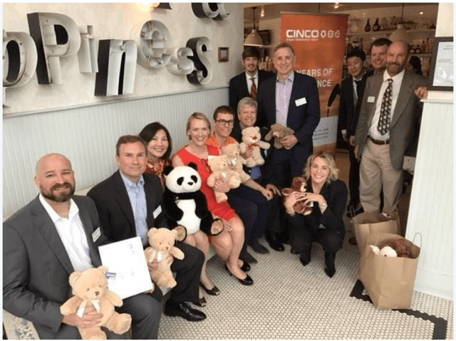 cinco team smiling holding stuffed animals at charity event 